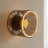 Bombilla LED donut E27 de cristal ahumado, Ø 120 mm, encendida como aplique de pared sobre una pared lisa y neutra