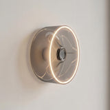 Bombilla LED donut E27 de cristal ahumado, Ø 195 mm, encendida como aplique de pared sobre una pared clara y sobria