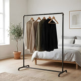 Burro de ropa industrial de tubos de fontanería negros en un dormitorio luminoso, ropa en perchas de madera
